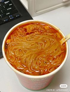 a bowl of noodles with chopsticks in front of a laptop computer on a desk