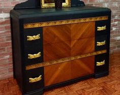 a black and gold dresser with a mirror on it's top, in front of a brick wall