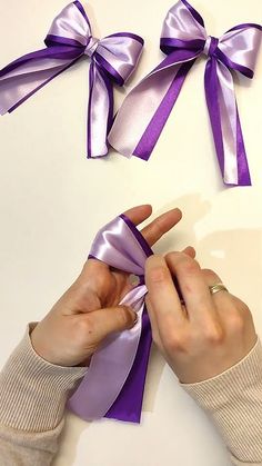 two hands are holding purple bows on a white surface