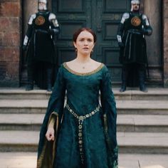 a woman in a green dress standing on steps with other people wearing black and gold