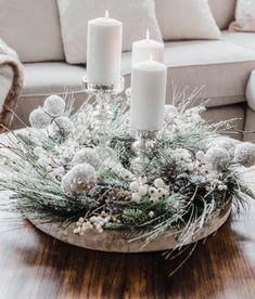 two candles are lit on top of a christmas centerpiece with pine cones and white balls