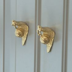 two gold hooks are attached to the side of a white door, one has a bird on it's head