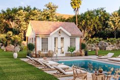 a pool house with lounge chairs around it and a swimming pool in the foreground