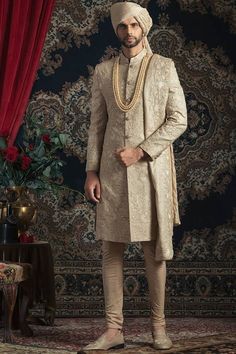 a man standing in front of a red curtain wearing a turban and white suit