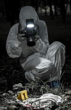 a person in a white suit holding a camera and kneeling on the ground with other items