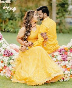 a man and woman in yellow sitting on a flower covered bench with flowers around them