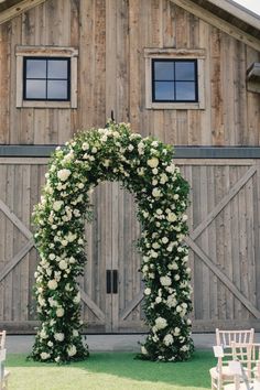 an arch covered in white flowers next to a barn