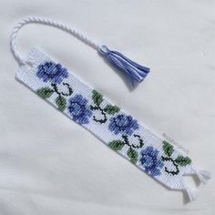 an embroidered bookmark with blue flowers and green leaves on white fabric, next to a tassel