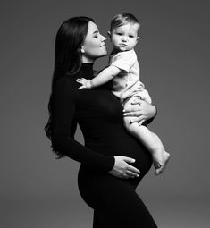 a woman holding a baby in her arms and looking at the camera while wearing a black dress