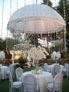 an outdoor dining area with tables, chairs and an umbrella over the table is decorated with white flowers