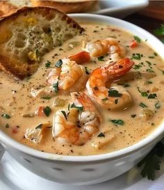 a bowl of soup with shrimp and bread on the side