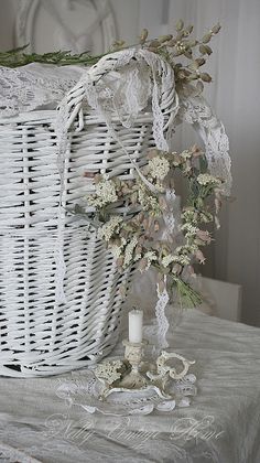 a white wicker basket with flowers and candles on a table next to a candle holder