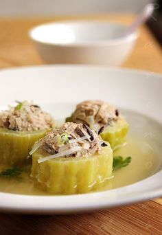 some food on a white plate sitting on a wooden table next to a bowl and spoon