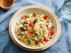 a white bowl filled with pasta salad next to a wooden spoon and glass of water