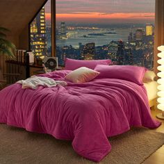 a bed with pink sheets and pillows in front of a large window overlooking the city