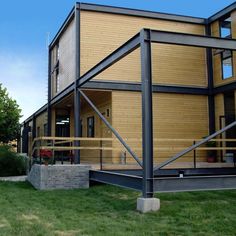 a modern home with wood siding and metal railings on the front porch, grass area