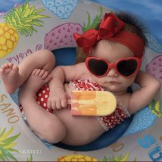 a baby with sunglasses and a red bow laying in a pool float holding a popsicle