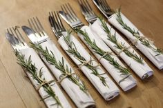 napkins wrapped in twine and tied with rosemary are lined up on a wooden table