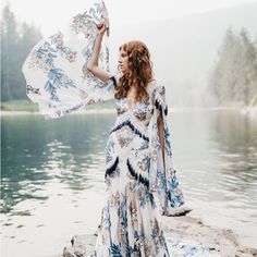 a woman in a blue and white dress is standing by the water