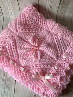 a pink knitted blanket with bows on it sitting on top of a wooden floor