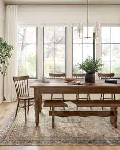 a dining room table with two chairs and a bench in front of the large windows