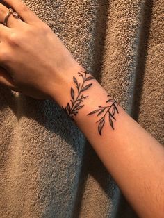 a woman's hand with a tattoo on her left wrist and an olive branch on the other arm