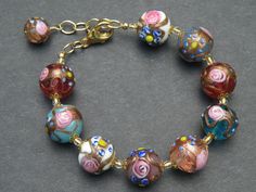 "The Fiorato (flower) beads, that some people call \"wedding cake beads\", on this bracelet, are Vintage Murano Glass Beads. This type of handmade, lamp worked Murano glass, Venetian Beads, are some of the first beads I ever bought in Venice, Italy. The assortment of 14-15 mm, round beads were made one-by-one under the flame. The glass maker starts with a Murano glass cane (or rod) to make the base color, and then adds an Aventurina (copper filings), band around the center of the bead. Next the Elegant Round Beads Bracelets For Celebrations, Elegant Single Strand Multicolor Beaded Bracelets, Multicolor Round Beads Bracelets For Weddings, Elegant Beaded Bracelets With Large Beads For Wedding, Elegant Multicolor Beaded Bracelets For Wedding, Round Polished Beads Bracelet For Wedding, Polished Round Bead Bracelets For Weddings, Wedding Beaded Bracelets With Spacer Beads, Colorful Beaded Wedding Bracelets