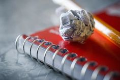 a red notebook with a crumpled ball of paper on top of it and a pencil