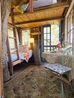 a room with a bed, table and chair in it next to a large window