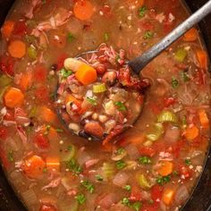 a spoon full of soup with carrots, celery and beans