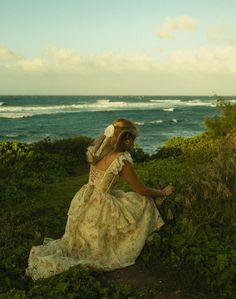 a woman in a dress is sitting on the grass by the ocean