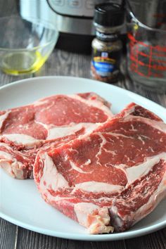 two pieces of raw meat on a white plate next to an instant pot roaster