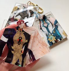 a hand holding three different anime keychains in front of a white table top