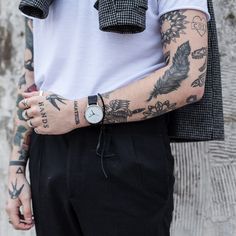 a man with tattoos on his arm and wrist is standing in front of a wall