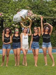 four women in black shirts and shorts are holding up a silver object while standing on the grass