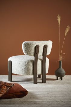 two chairs and a vase in front of a brown wall, with one sitting on the floor