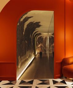 a woman is walking down the hallway in an orange and white room with black and white tiles on the floor