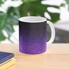 a purple and black coffee mug sitting on top of a table next to a book