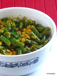 a white bowl filled with green beans and other vegetables on top of a red table