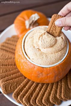 a hand dipping a cracker into a bowl of peanut butter on top of pumpkins