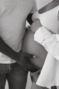 a pregnant woman holding her belly while standing next to a man in a white shirt