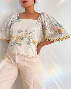 a woman standing in front of a wall wearing white pants and a top with flowers on it