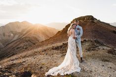 a bride and groom standing on top of a mountain at sunset with the sun behind them