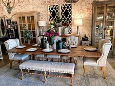 a dining room table and chairs in front of a brick wall with vases on it