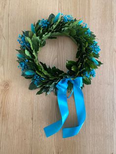 a blue ribbon tied around a wreath on top of a wooden table with leaves and flowers