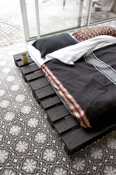 a bed made out of wooden pallets on top of a tiled floor next to a window