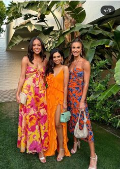 three beautiful women standing next to each other in front of some plants and trees with one woman holding a purse