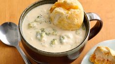 a bowl filled with broccoli and cheese soup next to a spoon on a wooden table