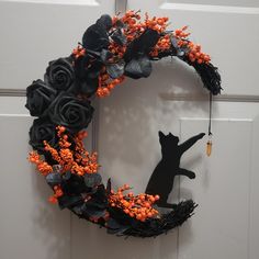 a black cat sitting on top of a wreath with orange flowers and leaves hanging from it