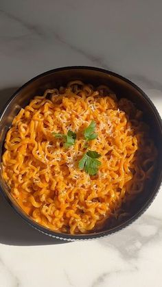 a bowl filled with noodles and parsley on top of a white countertop next to a spoon